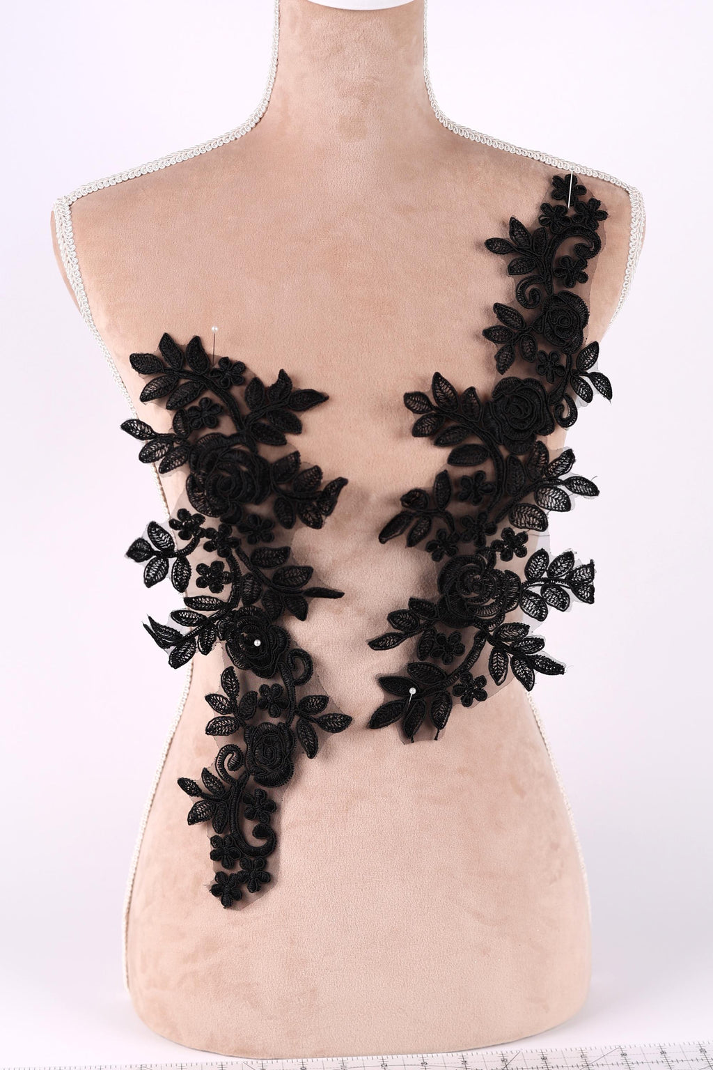 A mannequin torso with black lace appliques on it, featuring intricate floral and leaf designs.