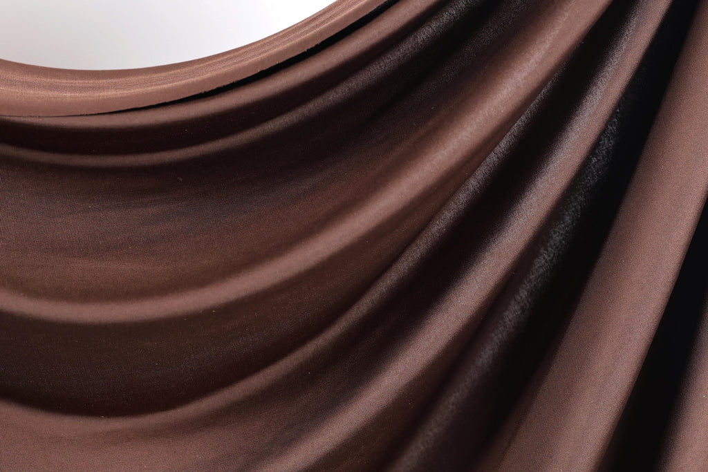 a close-up view of a brown, shiny fabric, possibly a piece of clothing or a textile. The fabric has a smooth, flowing texture and appears to be made of a shiny material, giving it a luxurious and elegant appearance.
