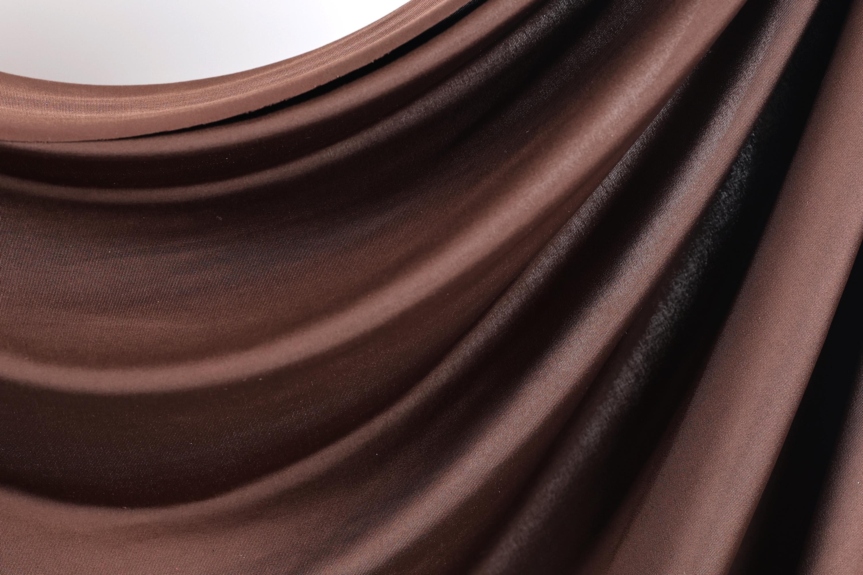 a close-up view of a brown, shiny fabric, possibly a piece of clothing or a textile. The fabric has a smooth, flowing texture and appears to be made of a shiny material, giving it a luxurious and elegant appearance.