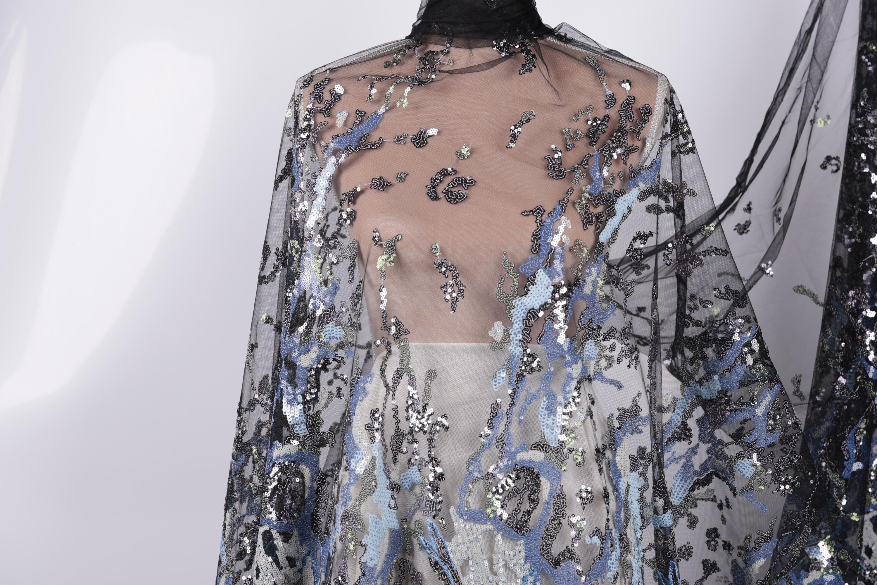 a close-up view of a sheer, black and blue sequined fabric draped over a mannequin.