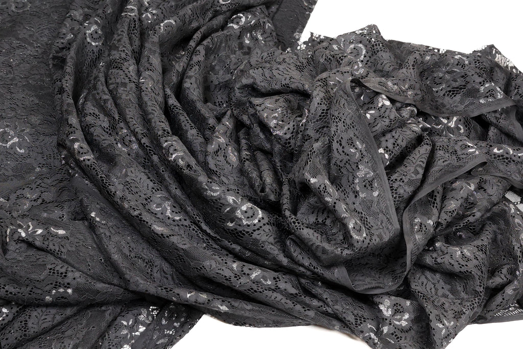 a close-up view of a black lace fabric with a floral pattern. The fabric appears to be crumpled and wrinkled, giving it a textured and somewhat messy appearance.