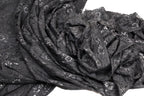 a close-up view of a black lace fabric with a floral pattern. The fabric appears to be crumpled and wrinkled, giving it a textured and somewhat messy appearance.