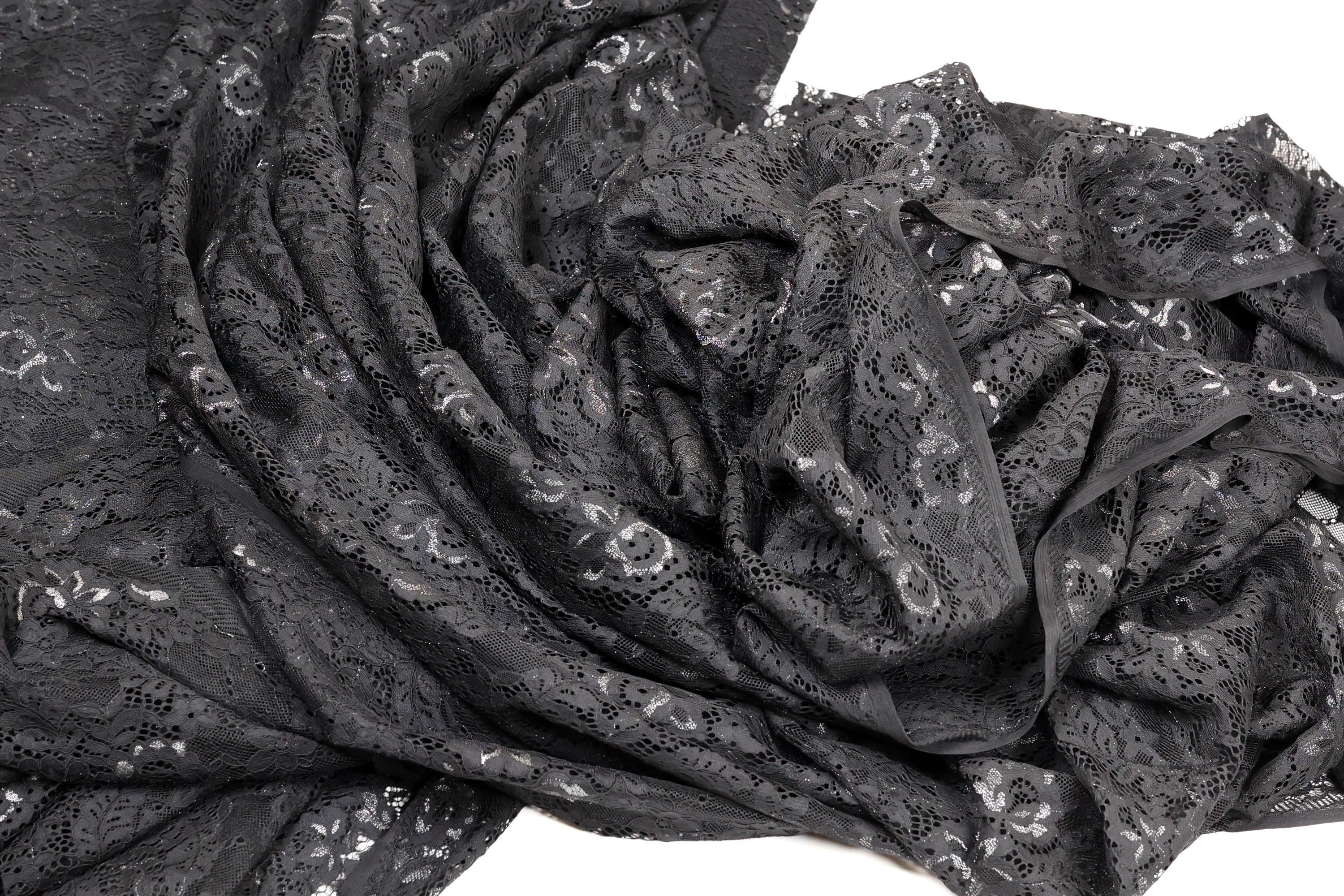 a close-up view of a black lace fabric with a floral pattern. The fabric appears to be crumpled and wrinkled, giving it a textured and somewhat messy appearance.