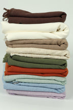 A stack of various colored towels or blankets, including white, brown, green, orange, and purple.