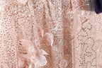 The image is a close-up of a delicate, pink and white sequined dress with intricate floral patterns.
