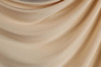 The image is a close-up of a light brown fabric, possibly a piece of clothing or a textile. The fabric appears to be soft and smooth, with a slightly wrinkled texture. The image does not contain any discernible objects or actions, and there are no specific details provided about the color or pattern of the fabric.