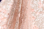 A close-up view of a delicate, pink sequined fabric with a floral pattern.