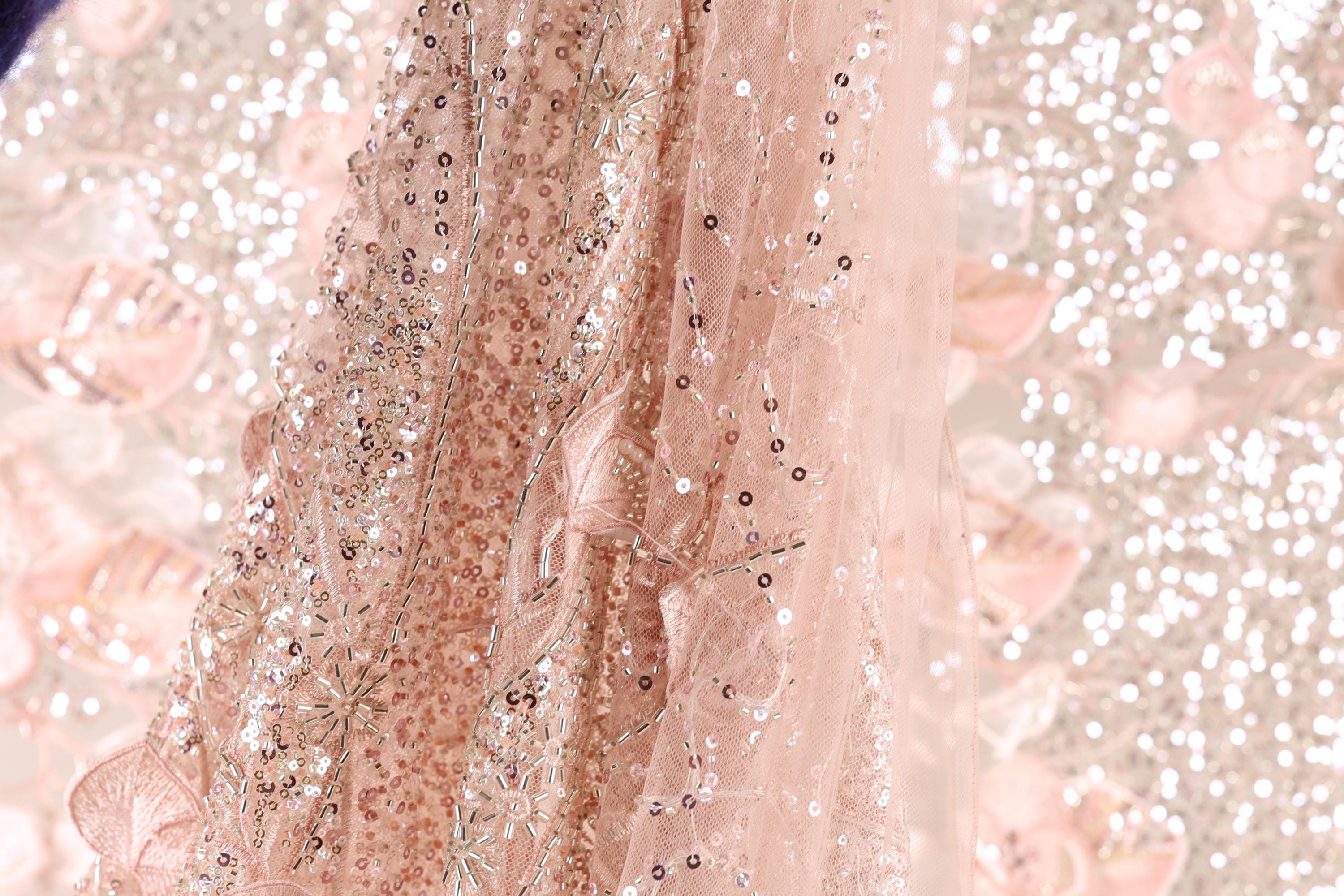 A close-up view of a delicate, pink sequined fabric with a floral pattern.
