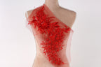 A mannequin wearing a red dress with a floral pattern on the shoulder.
