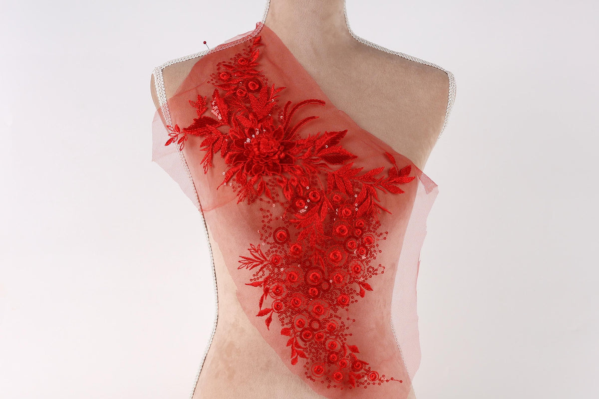 A mannequin wearing a red dress with a floral pattern on the shoulder.