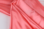 A close-up view of a soft, shiny pink satin fabric, with a smooth and flowing texture.