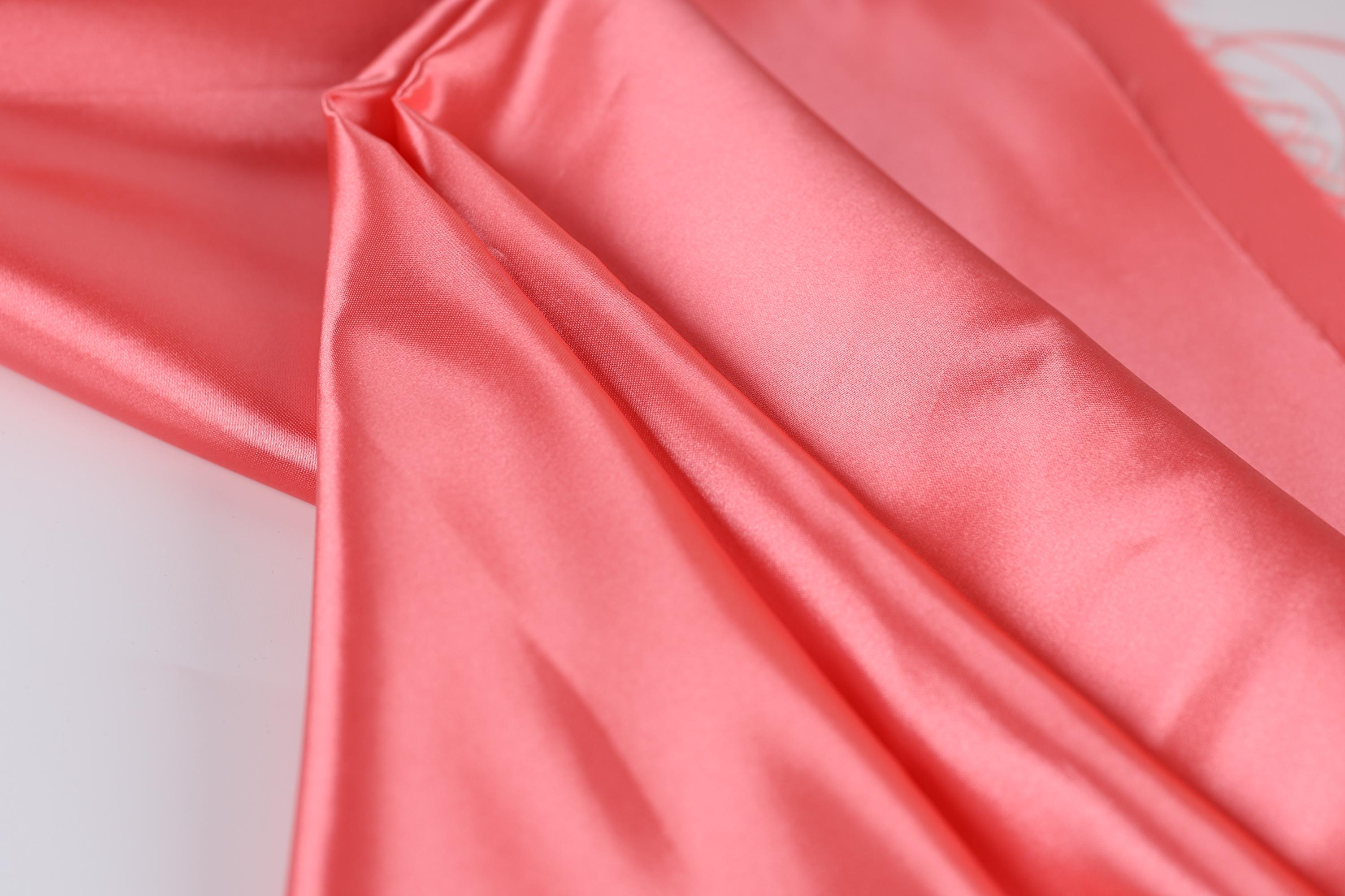 A close-up view of a soft, shiny pink satin fabric, with a smooth and flowing texture.