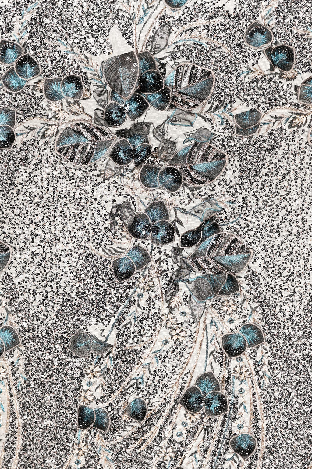 a close-up view of a fabric with a floral pattern. The pattern consists of various shades of blue and gray, with some areas appearing more vibrant and others more muted. The fabric appears to be a type of lace or textile, with a textured surface that adds depth and visual interest to the overall design.