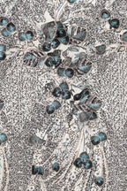 a close-up view of a fabric with a floral pattern. The pattern consists of various shades of blue and gray, with some areas appearing more vibrant and others more muted. The fabric appears to be a type of lace or textile, with a textured surface that adds depth and visual interest to the overall design.