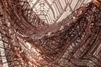 a close-up view of a fabric with a metallic, sequined texture. The fabric appears to be a dark brown color, with a pattern of small, shiny beads or sequins covering it. The fabric is crumpled and wrinkled, giving it a textured, three-dimensional appearance.