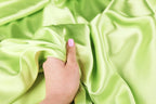 A hand with painted fingernails is holding a piece of green satin fabric.