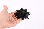 A hand holding a black flower against a white background.