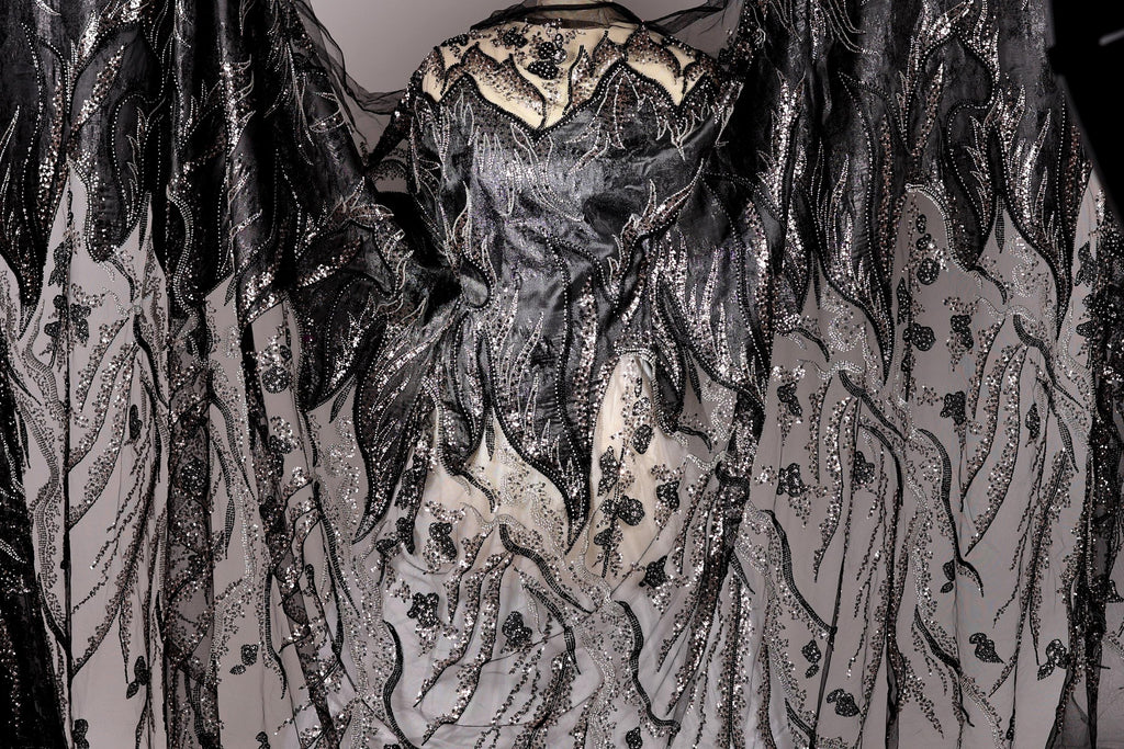 a black and white dress with intricate, detailed embroidery and sequinwork. The dress appears to be a formal or evening gown, with a flowing, draped silhouette. The design is visually striking and eye-catching, with the contrasting black and white colors creating a dramatic effect.