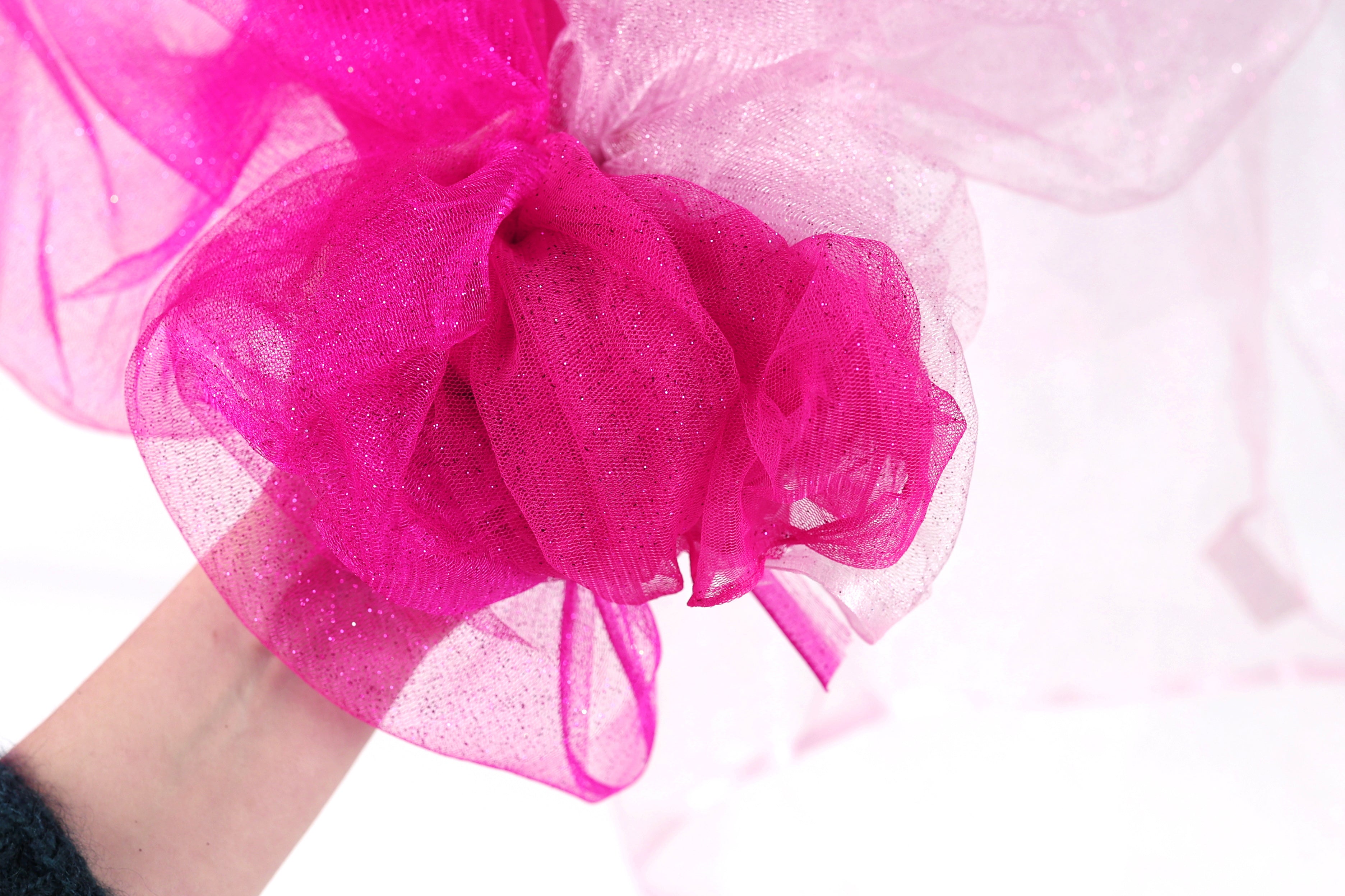 A hand holding a pink, sparkly fabric or material.
