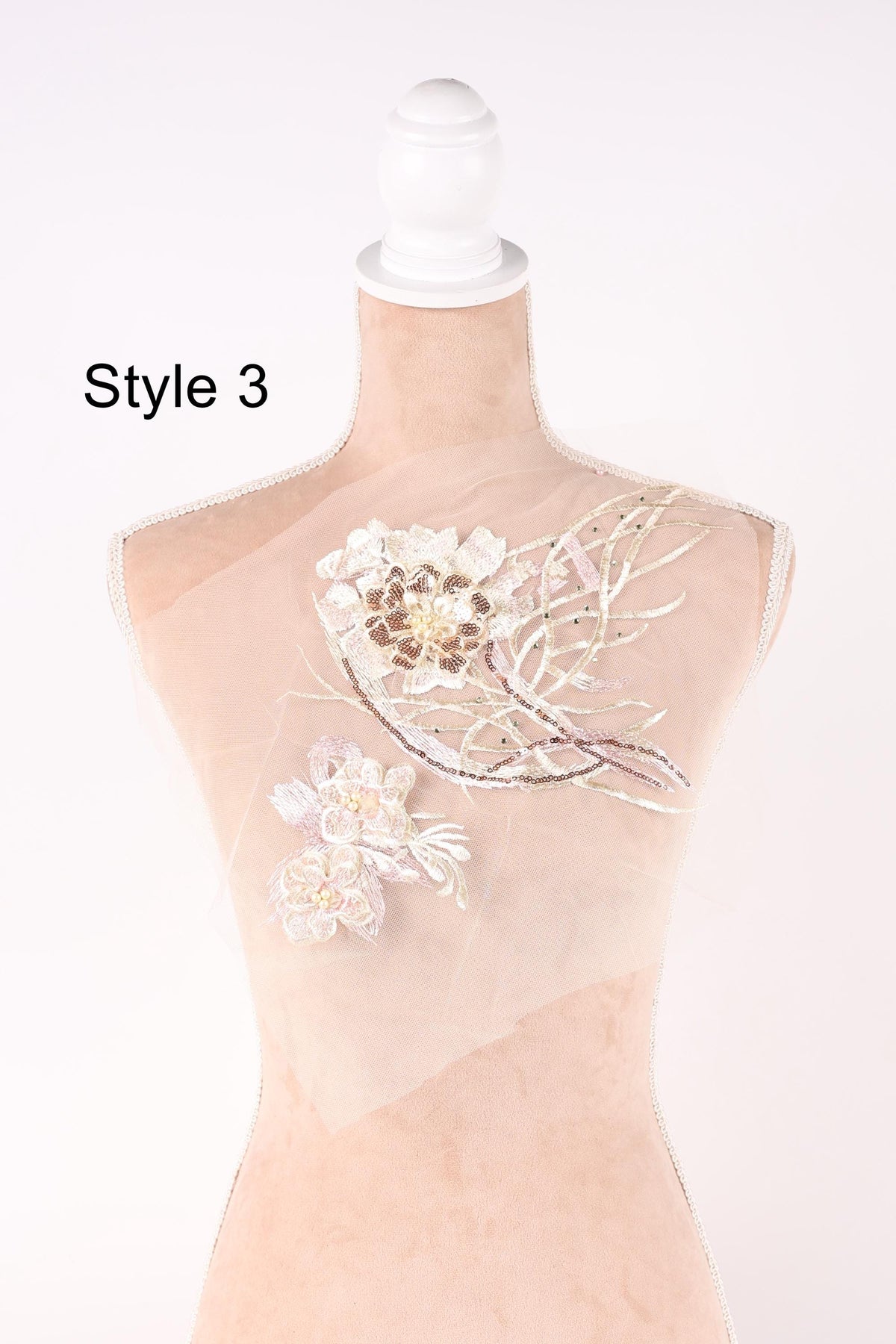 A mannequin with a white head and a beige body, adorned with delicate floral embroidery.