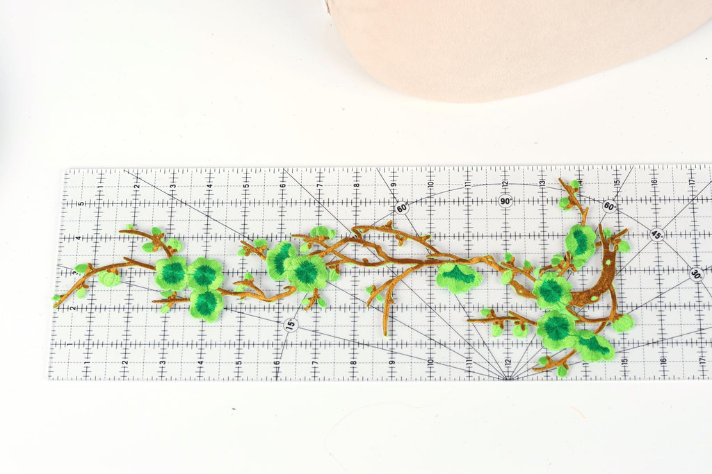 a close-up view of a white ruler with green floral embroidery designs on it.