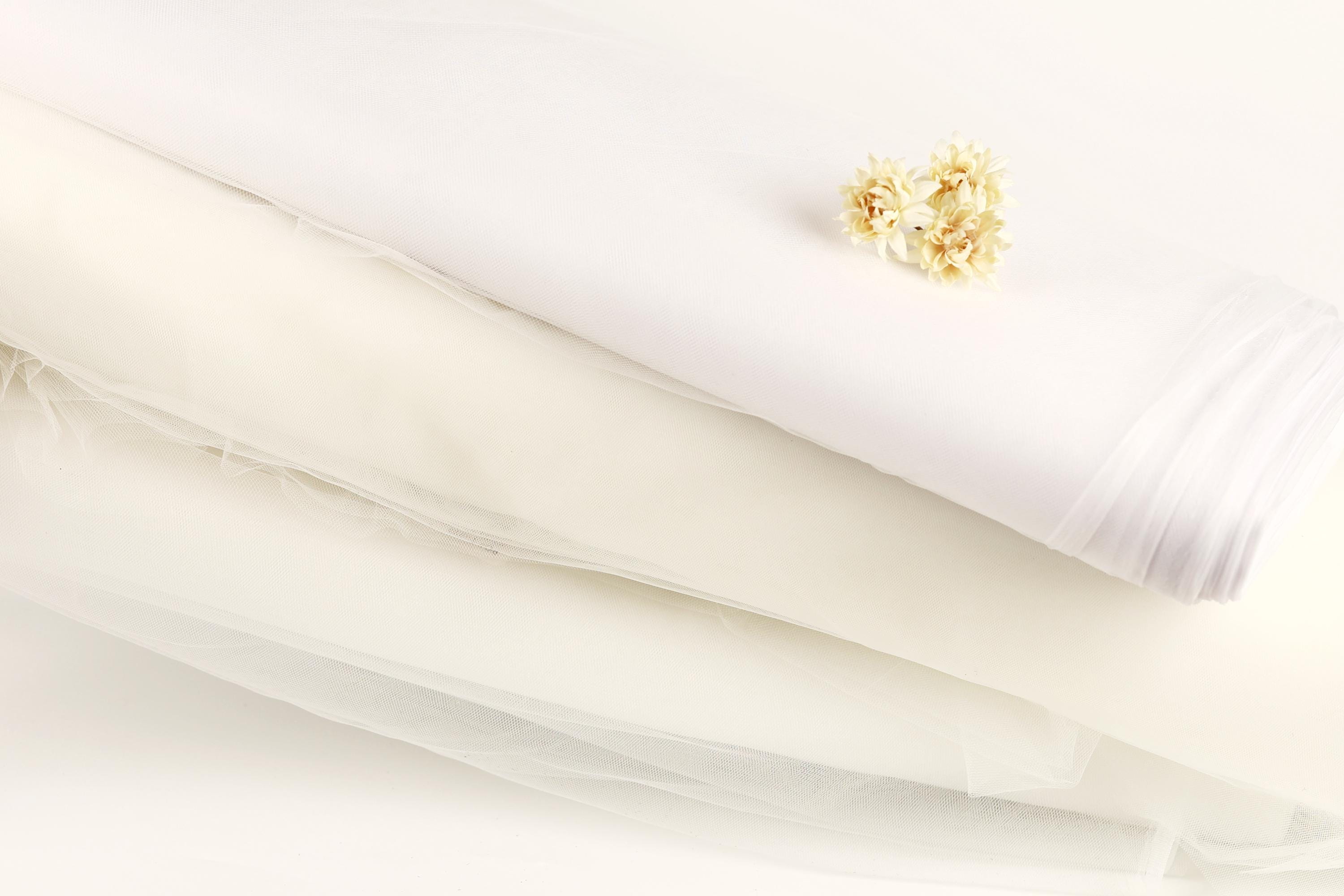 a white fabric, possibly a wedding dress, with a small yellow flower resting on top of it.
