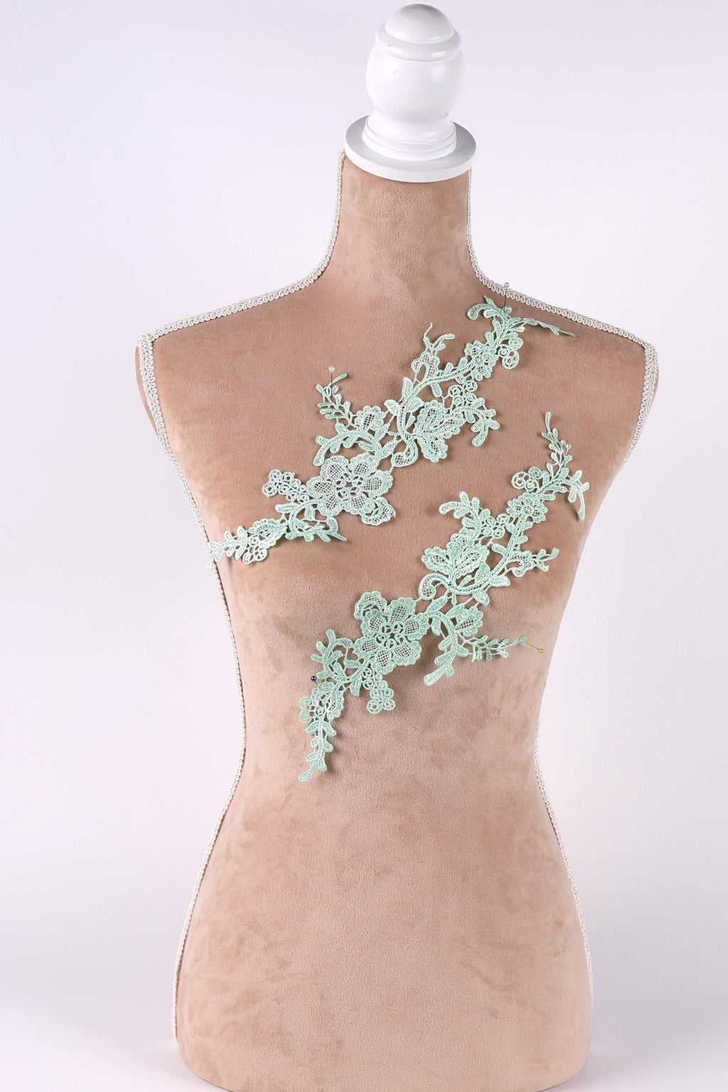 A mannequin with a light brown body and a white head, wearing a green lace dress with a floral pattern.