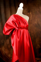 A red one-shoulder dress with a draped, flowing silhouette is displayed on a mannequin against a dark background.