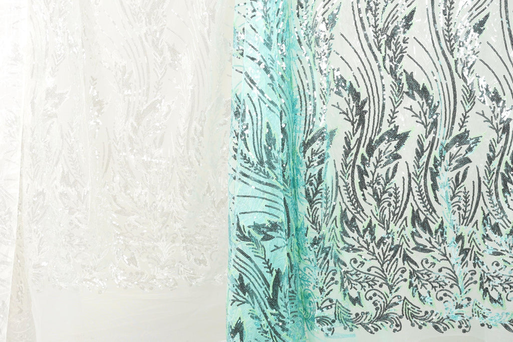 a close-up view of two fabric pieces with intricate patterns. The fabric on the left is white, while the fabric on the right is teal. The patterns on both fabrics are similar, with a floral or leaf-like design. The image does not contain any text or additional objects, and the focus is solely on the two fabric pieces.