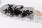 a piece of black fabric with intricate floral designs, placed on a transparent surface. Next to the fabric, there is a small piece of light-colored material, possibly a piece of paper or a small object.