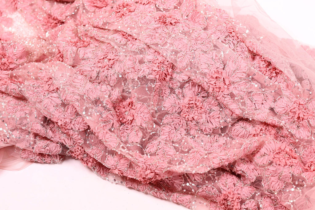 a close-up view of a delicate, pink fabric with a floral pattern. The fabric appears to be made of a soft, sheer material and has a delicate, intricate design with small, overlapping flowers or petals. The fabric is not a single piece but rather a collection of individual fabric pieces that come together to create the overall pattern.