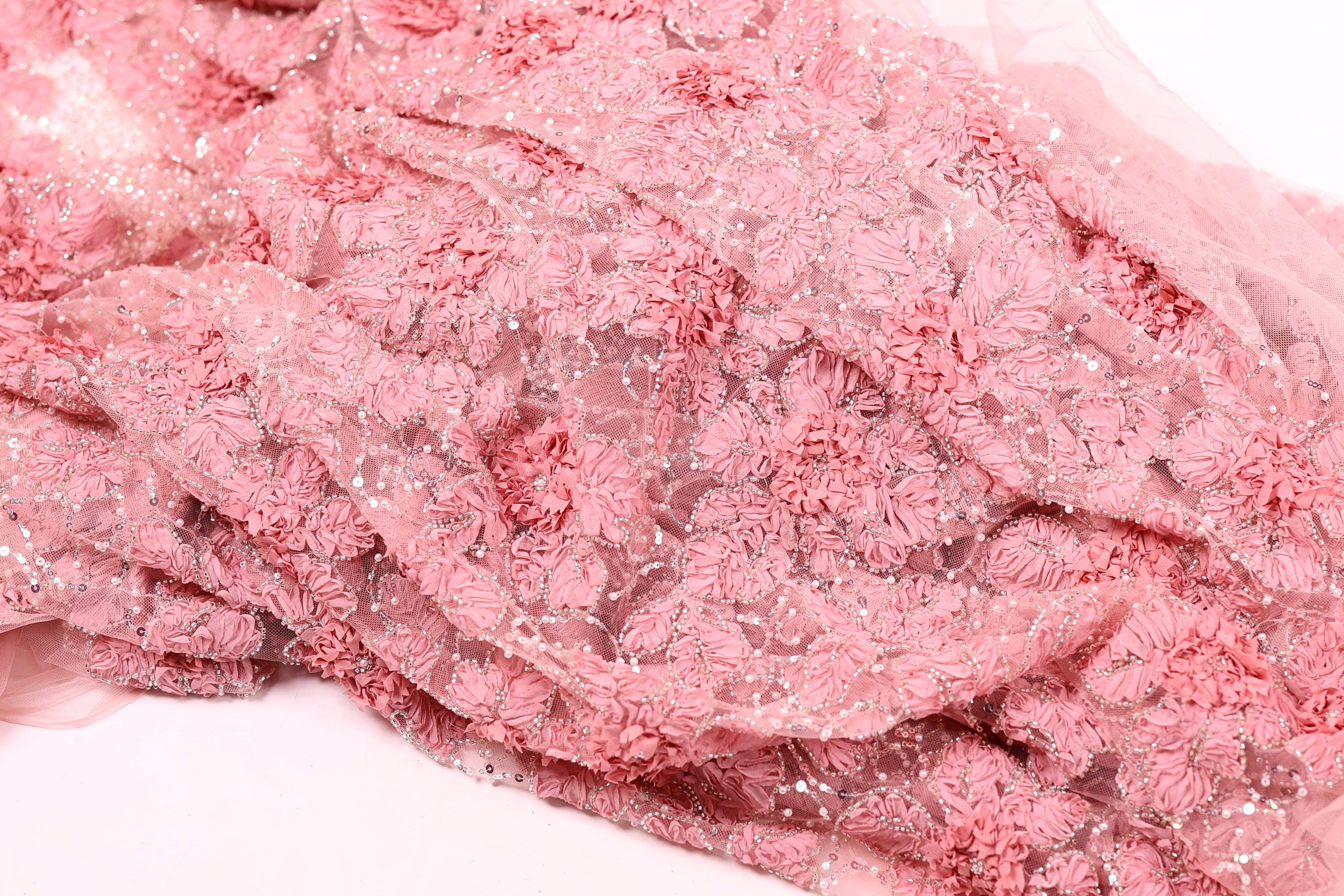 a close-up view of a delicate, pink fabric with a floral pattern. The fabric appears to be made of a soft, sheer material and has a delicate, intricate design with small, overlapping flowers or petals. The fabric is not a single piece but rather a collection of individual fabric pieces that come together to create the overall pattern.
