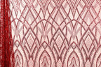 a close-up view of a fabric with a repeating pattern of red sequin designs. The pattern consists of various shapes and lines, creating a visually striking and intricate design. The fabric appears to be a pink or peach-colored material, which contrasts with the red sequin pattern. The image does not contain any text or other discernible objects, and the focus is solely on the fabric and its design.