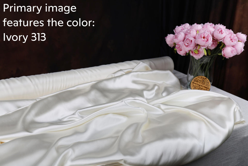 a white satin fabric with a vase of pink peonies on a table.