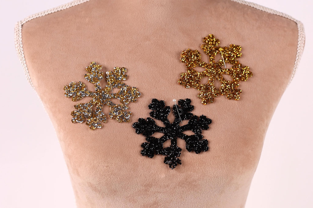 three snowflake-shaped embellishments on a mannequin's torso, with two gold-colored snowflakes and one black-colored snowflake.