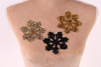 three snowflake-shaped embellishments on a mannequin's torso, with two gold-colored snowflakes and one black-colored snowflake.