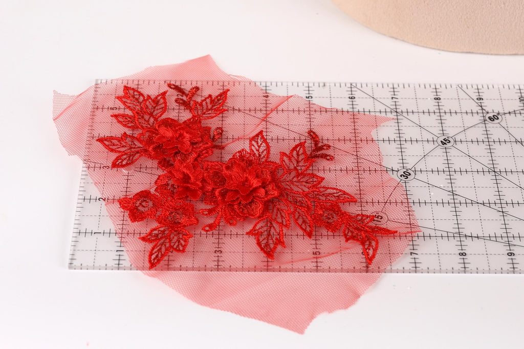 a red floral lace piece placed on a transparent ruler, which is lying on a white surface.