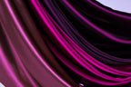 a close-up view of a fabric with a gradient of colors, including shades of purple and pink. The fabric appears to be made of silk or satin, and it is folded or draped in a way that creates a visually striking and textured appearance.