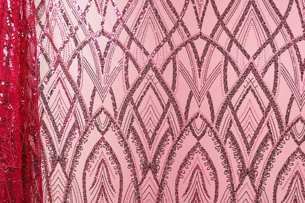 a close-up view of a pink fabric with a repeating pattern of black and pink sequin designs. The pattern is intricate and visually striking, with the sequins adding a touch of sparkle and texture to the fabric.