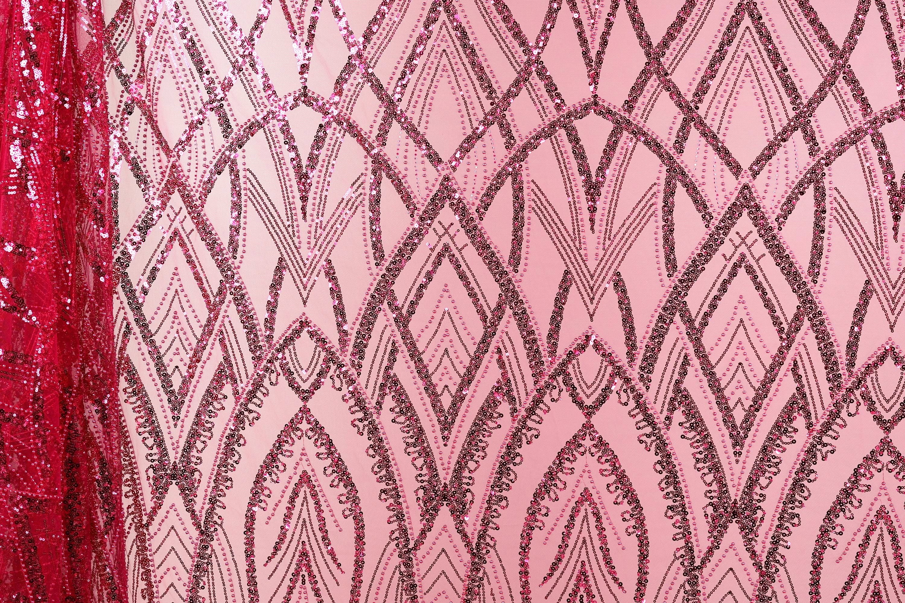 a close-up view of a pink fabric with a repeating pattern of black and pink sequin designs. The pattern is intricate and visually striking, with the sequins adding a touch of sparkle and texture to the fabric.