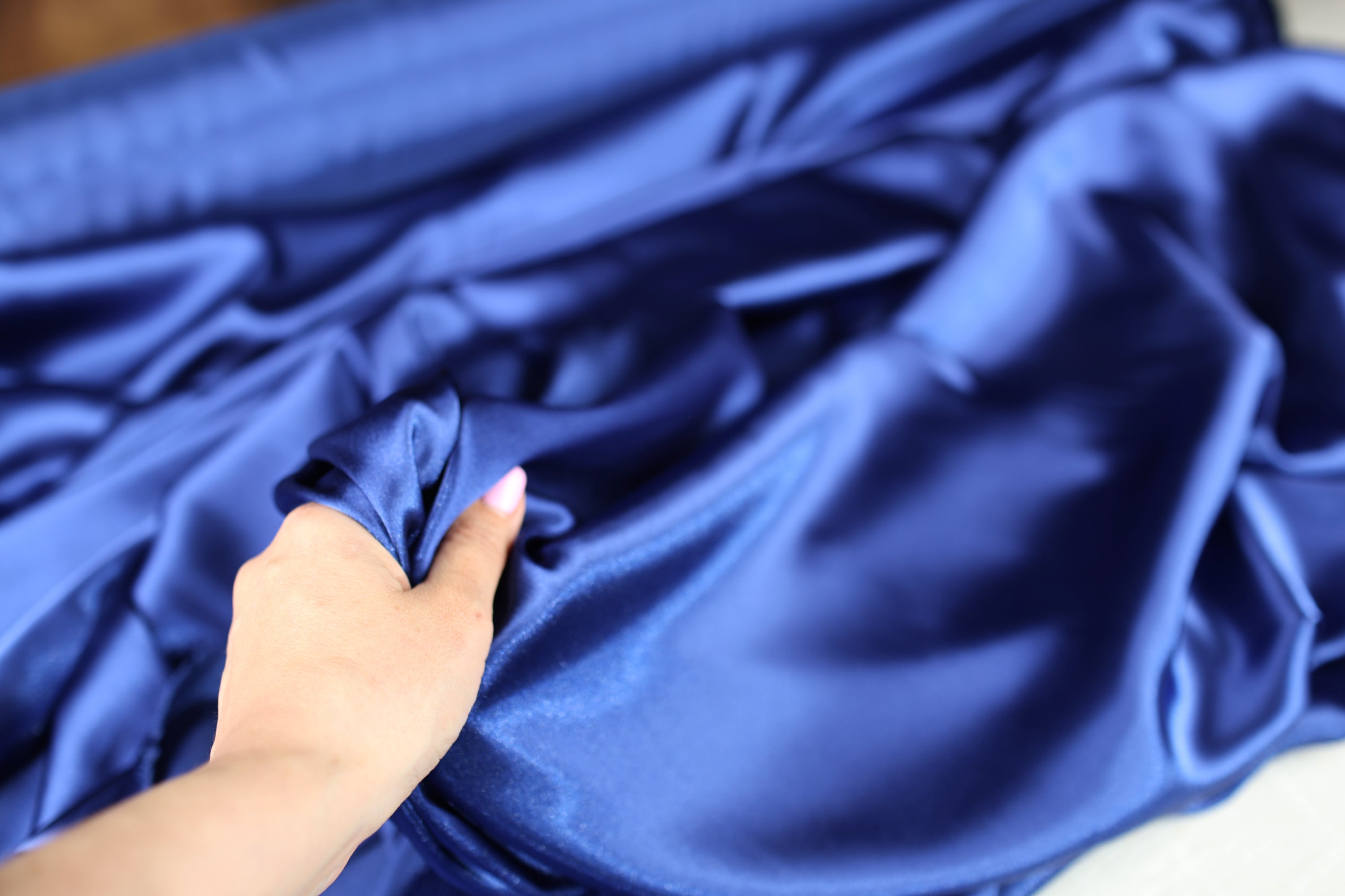 A hand is holding a piece of blue satin fabric, examining it closely.