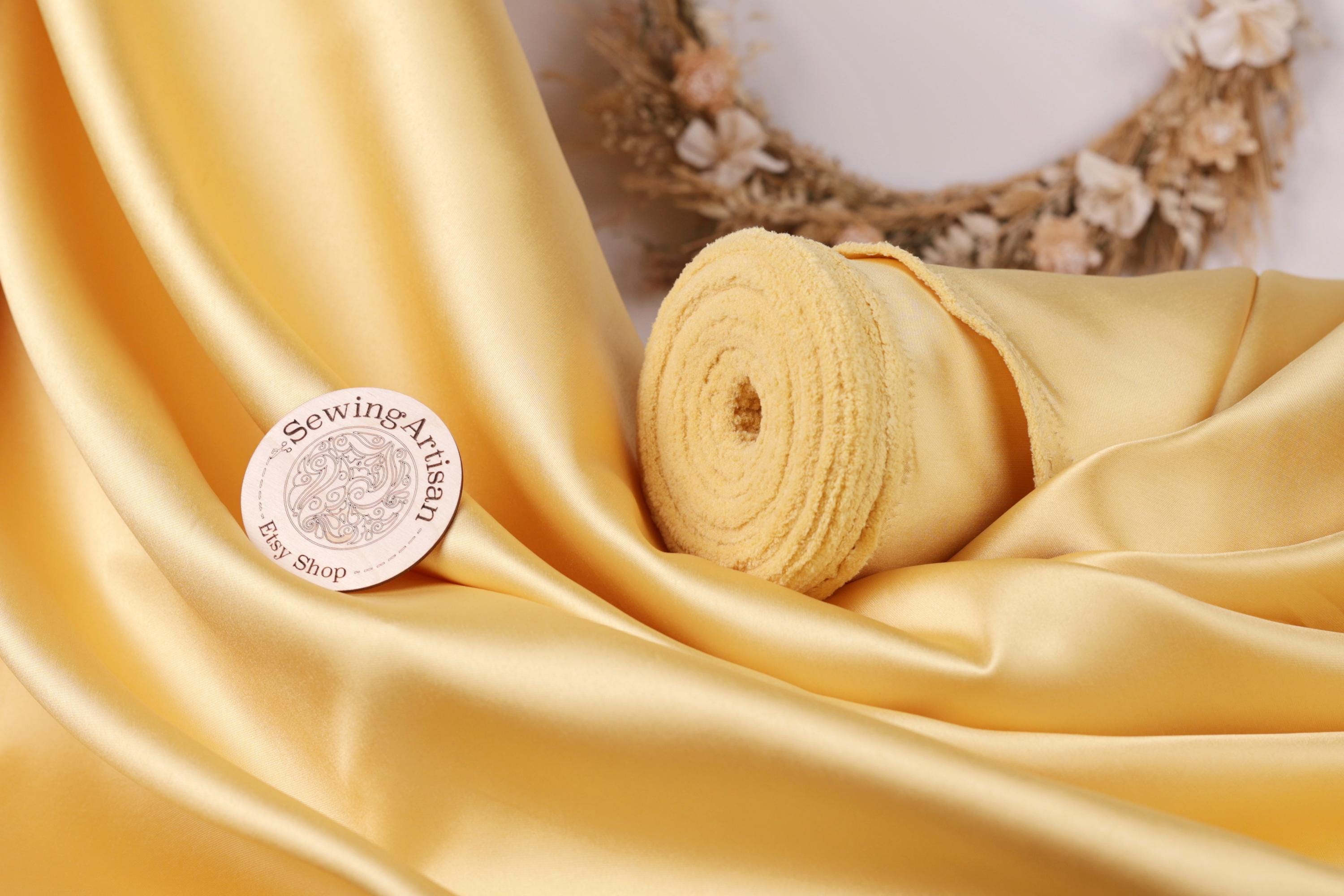 a yellow fabric with a sewing machine logo, a rolled-up yellow fabric, and a wreath with flowers in the background.