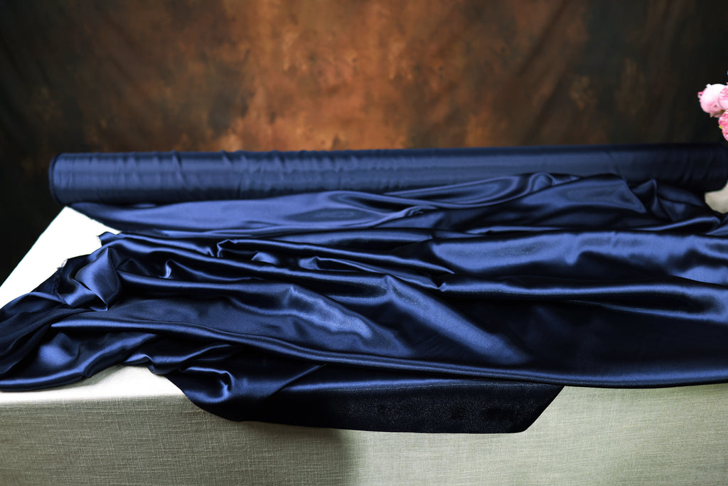 a roll of blue satin fabric on a table, with a dark background.