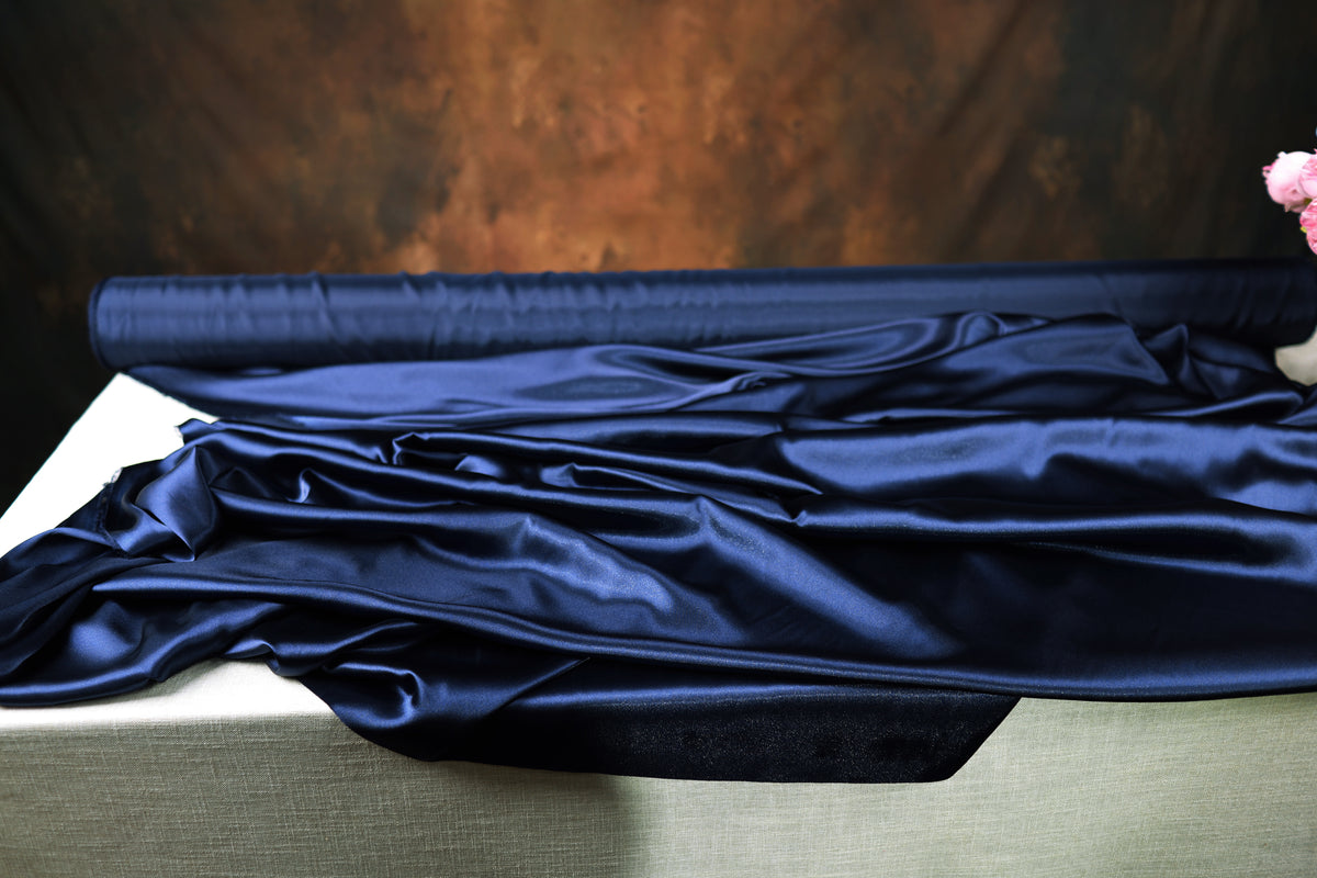 a roll of blue satin fabric on a table, with a dark background.