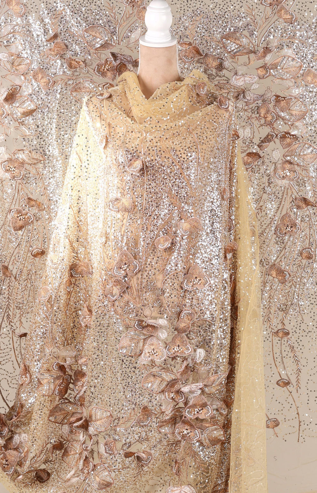 a mannequin wearing a gold and beige sequined dress with a floral pattern.