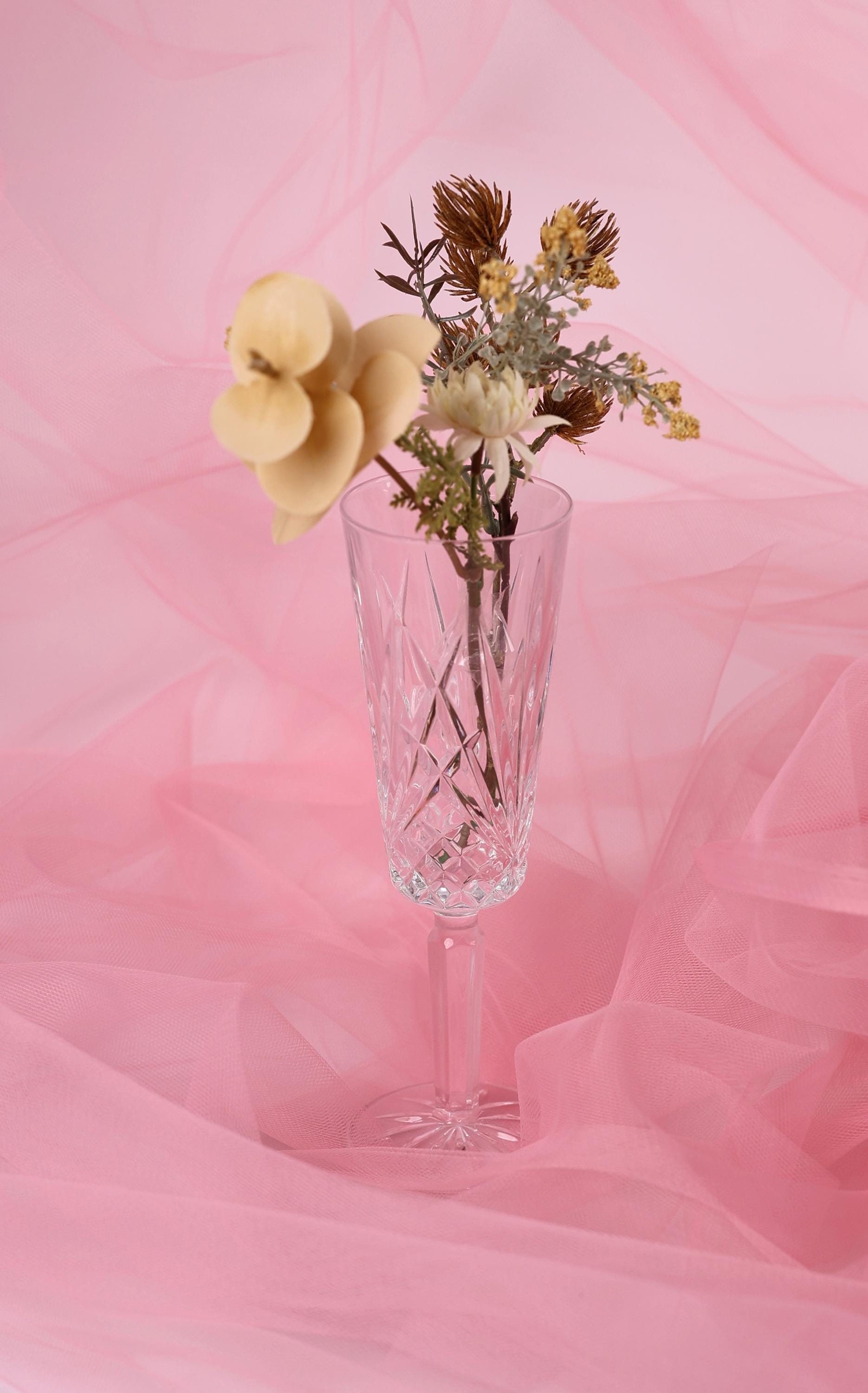 A clear glass vase filled with a bouquet of flowers sits on a pink background.