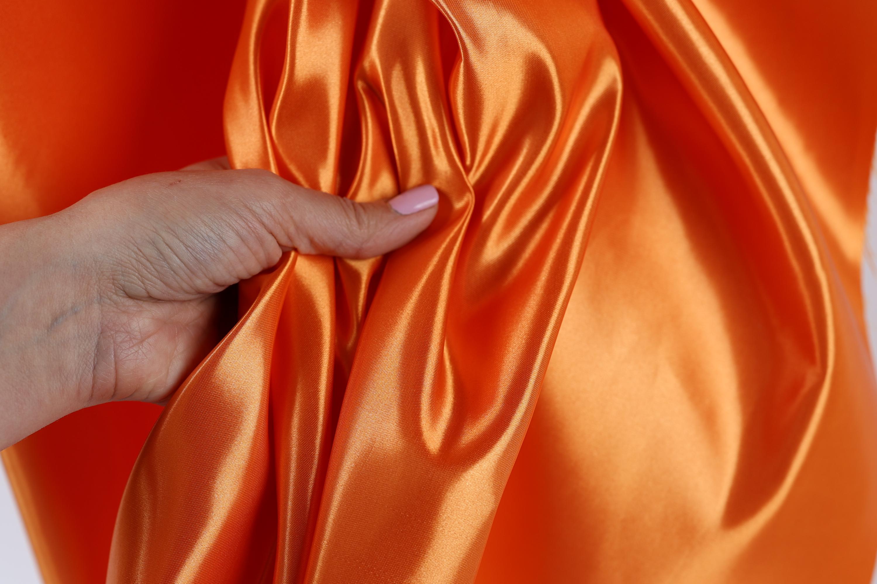 A hand is holding a piece of orange satin fabric, with the fabric partially draped over the hand.