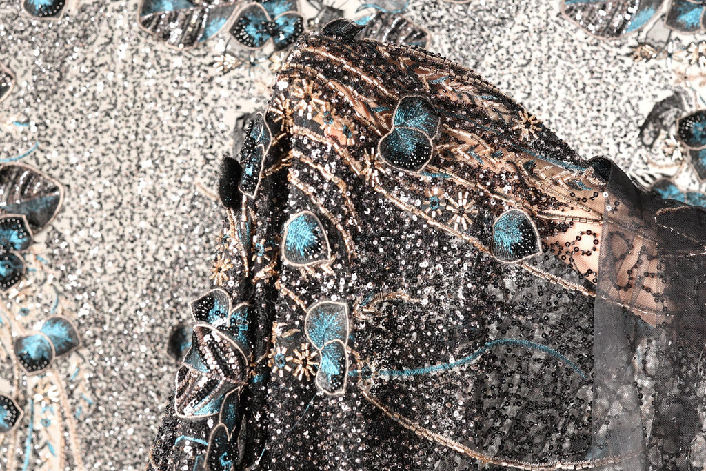 a close-up view of a black and gold sequined fabric with intricate floral and leaf designs.