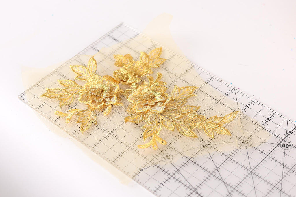 a close-up view of a piece of paper with a clear ruler on it, displaying a pattern of gold embroidered flowers.