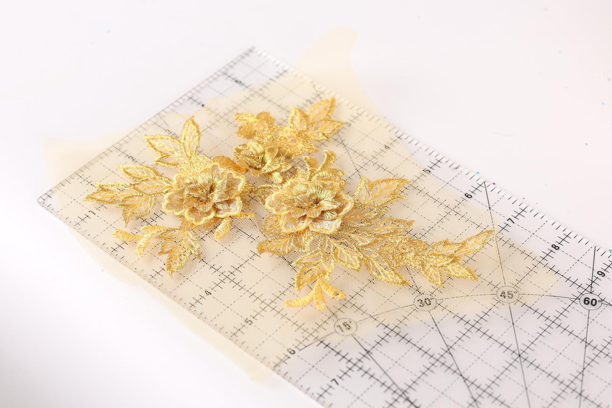 a close-up view of a piece of paper with a clear ruler on it, displaying a pattern of gold embroidered flowers.